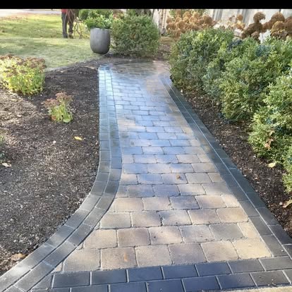 A curved tumbled-paver walkway winding through planted beds.